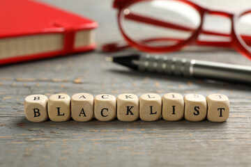Cubes with word Blacklist and office stationery on grey wooden desk, closeup