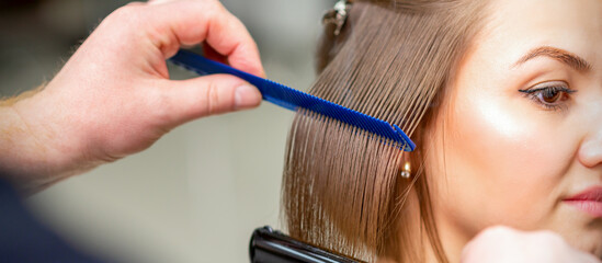 Hairdresser straightens female brown hair of medium length with a hair with an iron hair...