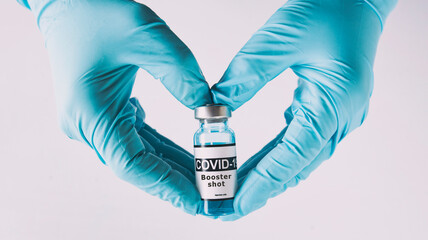 The shape of heart made from hands in gloves holding the covid vaccine booster shot