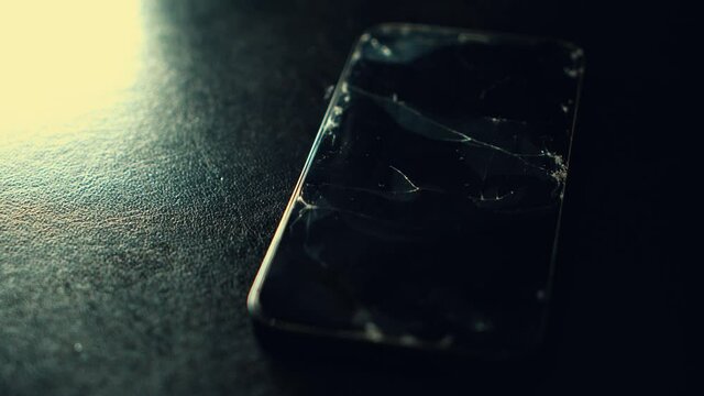 Broken glass screen smartphone on a black textured background. Twinkling blinking light. Cracked glass on a screen. Crash phone, fractured, repair, regret concept. Selective focus, close up, 4K