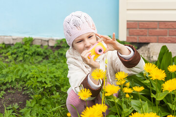 a girl in the spring photographs yellow daisies on the street with a children's camera