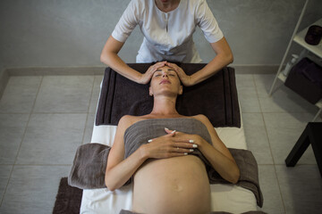 Female hands of therapist doing face massage to pregnant girl with spa salon, professional relaxing massage during pregnancy, pregnant woman body care, spa therapy