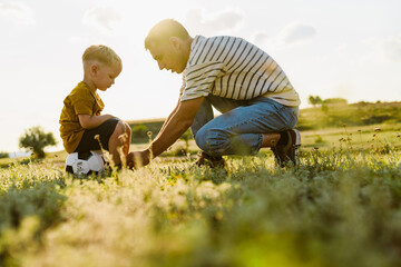 Naklejka na ściany i meble Young white father talking with her sad son while squatting on field