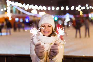 Young beautiful woman in knitted hat and scarf standing in the city with bengal light, sparkler. Concept celebration and christmas.