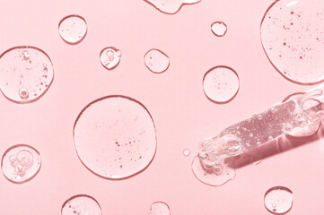Drops of anti-aging emulsion and glass pipette tip on light pink surface close upper view. Skincare...