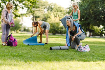 Multiracial women unrolling their mats during yoga practice in park