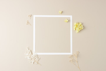 Cosmetic background with flowers and white frame on pastel beige. Flat lay, copy space