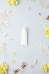 White tube of cosmetic cream with flowers on grey background. Flat lay