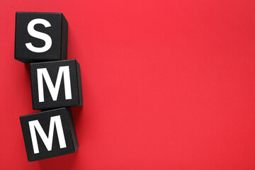 Black cubes with abbreviation SMM (Social media marketing) on red background, flat lay. Space for...
