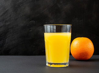 orange juice in a glass with fresh orange on a dark background