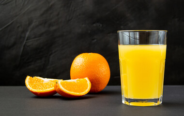 orange juice in a glass with fresh orange and chopped slices on a dark background