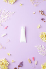 White tube of cosmetic cream with flowers on rose background. Flat lay