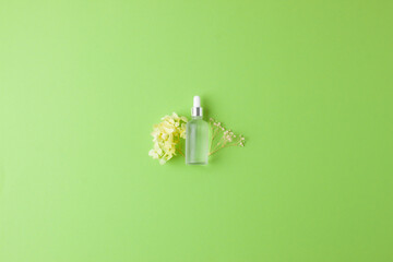 Cosmetic bottle with flowers on green background. Flat lay, copy space