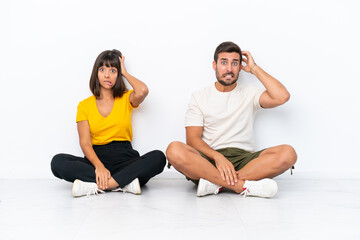 Fototapeta na wymiar Young couple sitting on the floor isolated on white background takes hands on head because has migraine