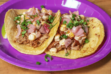 Traditional Mexican tacos with meat and vegetables in purple paper plates served for takeaway on wood table. Mexican food background.