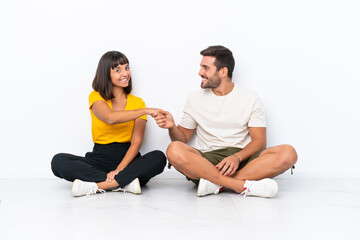 Young couple sitting on the floor isolated on white background handshaking after good deal