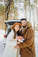 Smiling couple with beige dog sitting in open SUV car trunk in snowy forest. Enjoying each other in active winter holidays.