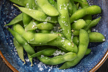 Organic steamed Japanese Edamame, a young soybean that is rich in nutrients served in blue bowl  and sprinkled with sea salt flakes. Vegetables Background. Healthy eating concept