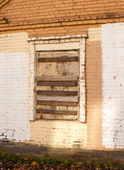Photo of a boarded up window of a brick house on the street