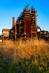 Obraz premium Ruined blast furnace industrial site in Dortmund Ruhr Basin Germany. Warm light of low autumn sun illuminating massive steel construction at lost place Phoenix-West amidst of upcoming vegetation.