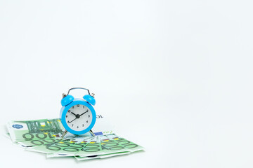 small blue clock on euro banknotes stands on a white background. The concept is time to make money, every minute bears money losses, every minute can be earned. Layout for inscriptions, copy space,