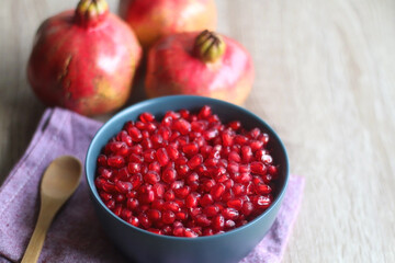 Bowl filled with pomegranate seeds and pomegranate fruit on a table. Selective focus.