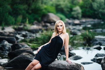 blonde girl in a black dress with blue eyes on the coast of the river