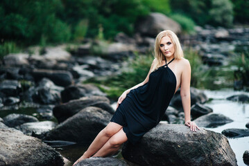 blonde girl in a black dress with blue eyes on the coast of the river
