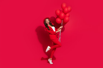 Photo of charming excited young woman wear suit jacket cap smiling holding balloons isolated red color background