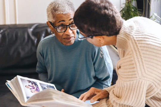 Elderly black woman looks at her adult daughter while they look at a photo album