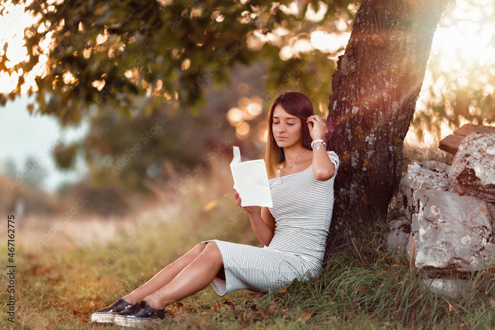 Sticker shallow focus of a caucasian female with a white dress posing in the park and reading a book