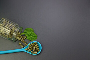 Green fusilli pasta in a blue spoon and fresh spinach leaves on a gray background. Spinach fusilli pasta. 