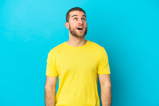 Young handsome caucasian man isolated on blue background looking up and with surprised expression
