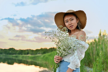 Young asian girl at sunset near the shore of the lake with a bouquet of wildflowers
