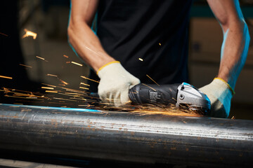 an angle grinder in male hands in gloves grinds a pipe with sparks