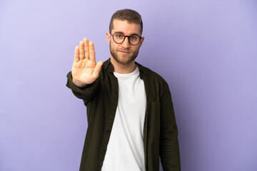 Young handsome caucasian man isolated on purple background making stop gesture