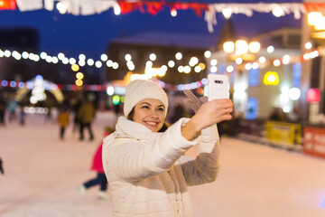 Happy young woman in winter on the ice rink taking picture on smartphone, selfie.