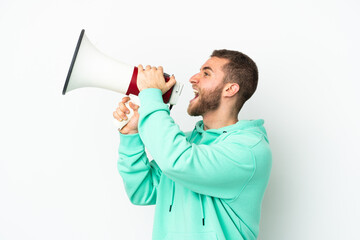 Young handsome caucasian man isolated on white background shouting through a megaphone to announce something in lateral position