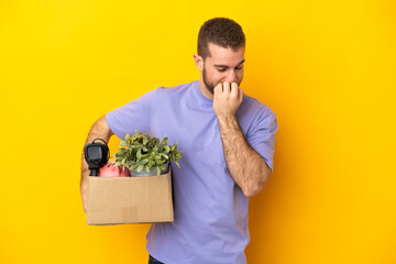 Young caucasian making a move while picking up a box full of things isolated on yellow background having doubts