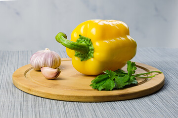 Yellow bell peppers, garlic and cilantro on a wooden cutting board. Vegetables ready for cooking. Healthy balanced nutrition, vegetarianism.