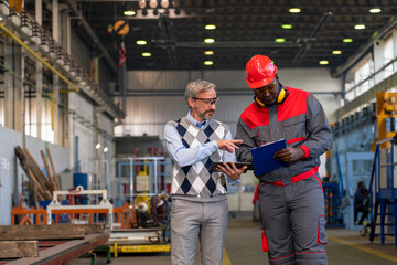 Caucasian Manager Giving Orders To Black Worker in Protective Workwear With Clipboard - Multiracial Industrial Co-Workers Standing In A Factory And Talking About Production Process