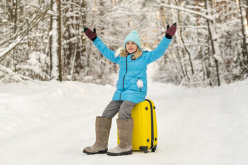 A girl in winter in felt boots sits on a suitcase on a frosty snowy day