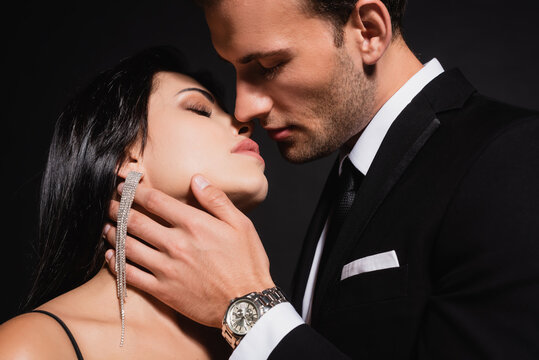 elegant man kissing brunette woman isolated on black