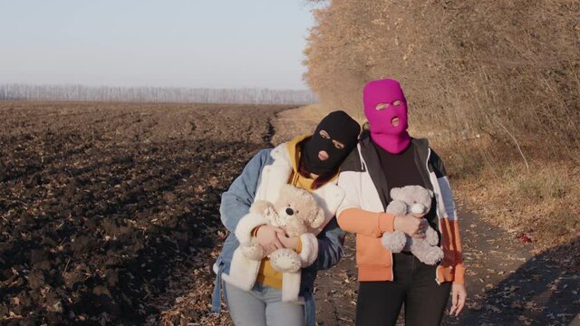 Women in balaclava with teddy bears outdoors. Hooligans in masks with plush toys in hands.