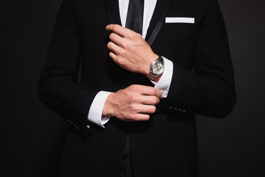 cropped view of elegant man in suit buttoning sleeve of white shirt isolated on black