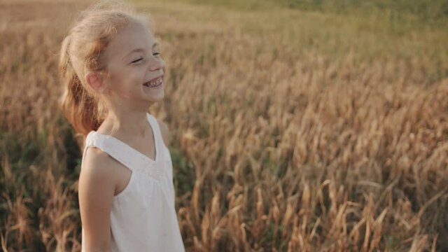 A joyful little girl with missing front teeth fooling around and grimaces at the camera at a family picnic in a wheat field. Slow motion