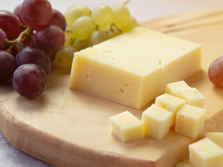 Light meal with sliced cheese next to a bunch of white and red grapes