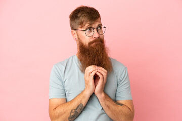 Young reddish caucasian man isolated on pink background scheming something