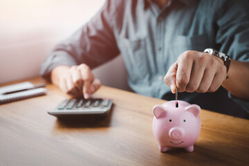 Obraz na płótnie Canvas A man hand putting coins in pink piggy bank for account save money. Planning step up, saving money for future plan, retirement fund. Business investment-finance accounting concept.