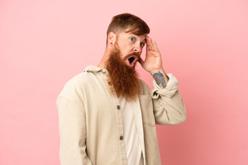 Young reddish caucasian man isolated on pink background doing surprise gesture while looking to the side